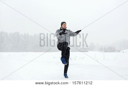 fitness, sport, people, exercising and healthy lifestyle concept - young man exercising and warmig up in winter outdoors