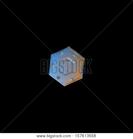 Snowflake isolated on black background. This is macro photo of real snow crystal: tiny hexagonal plate with relief central hexagon and simple pattern of six marks near of outer rim.