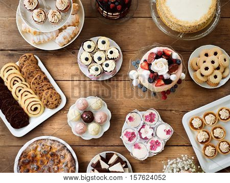 Table with cake, pies, cupcakes, tarts and cakepops. Studio shot on brown wooden background. Flat lay.