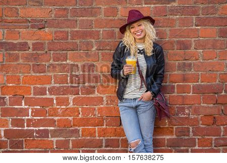 Modern woman standing by the brick wall with orange juice in her hands