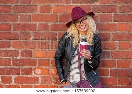 Modern woman having coffee while standing by the brick wall