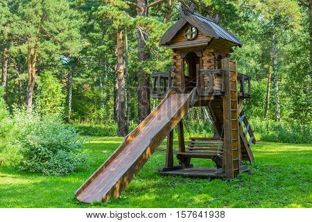 Wooden roller coaster from a fairy tale. Carved wood beautiful ornament a ladder and a swing under the slide. Playground on the meadow near the forest.