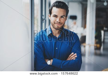 Portrait of successful confident hispanic businessman smiling and standing close from the window in modern office.Horizontal, blurred background