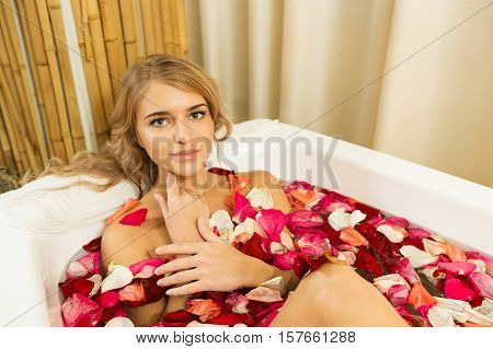 Young beautiful girl receives milk bath with rose petals in spa salon