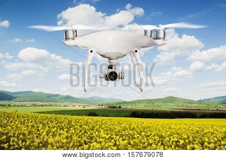 Close up of hovering drone taking pictures of yellow canola field, green hills and blue sky with white clouds