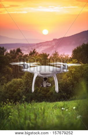 Close up of hovering drone taking pictures of green meadows and hills at sunset