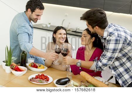 Group of happ young people sitting by the table eating and drinking red wine