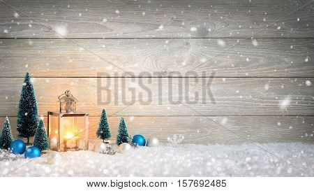 Christmas background with wooden board falling snow a burning candle in a lantern and ornaments