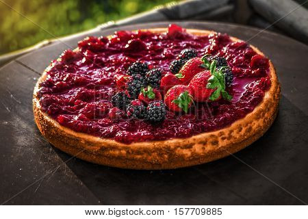 Delicious and fresh red berry fruits cheesecake on a wood plate with and cherries, strawberries