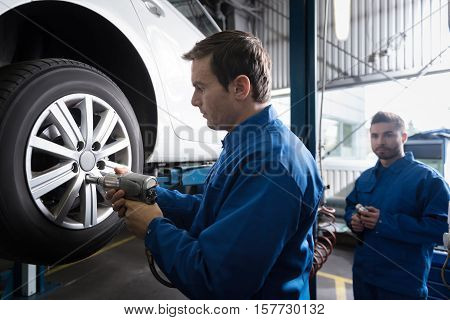 Concentrate on work. Professional experienced car mechanic using pneumatic wrench while chaning car wheel while working in auto service