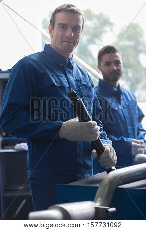 Work with inspiration.Professional delighted adult car mechanic holding tool and reparing car while working with his colleague in auti service