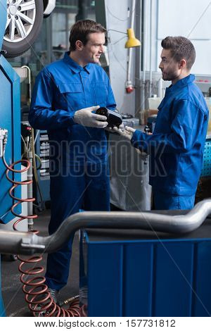 Brainstorming.Professional pleasant mechanics talking and holding tools while reparing car