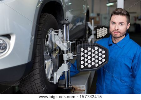 look it properly. Professional mechanic standing near car and adjusting automobile wheel alignment while working in service station