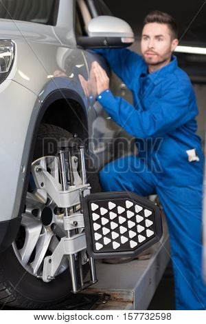 Concentrated on work. Selective focus of automobile wheel alignment system with professional mechanic standing in the background