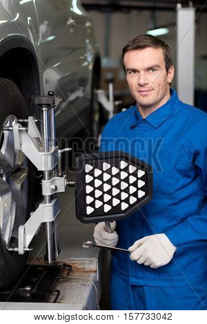 Conduct reparation. Pleasant professioanl mechanic holdign wrench and adjusting automobile wheel alignment while being involved in work