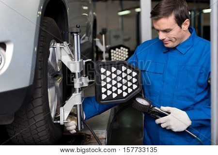 Involved in working day. Pleasant professional mechanic standing near car and checking automobile wheel alignment while working