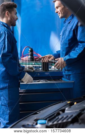 Share ideas. ositive prfessioal mechanics talking and resting after repairing car engine while being involved in work