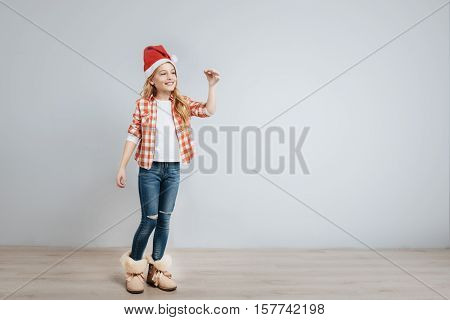 Happy holidays. Cheerful delighted little girl ringing bell and smiling while standing isolated on grey background