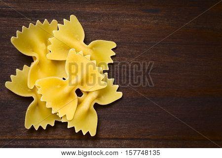 Raw farfalle or bow-tie pasta photographed overhead on dark wood with natural light (Selective Focus Focus on the top pasta)