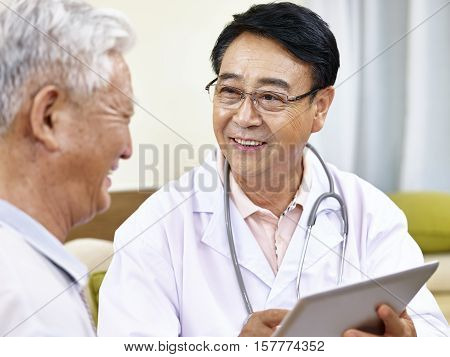 asian doctor using tablet computer to explain health condition to a senior patient happy and smiling