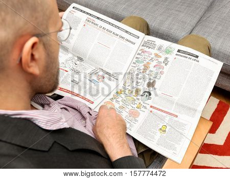 PARIS FRANCE - NOV 12 2016: Man reading Charlie Hebdo magazine on after Donal Trump elections as USA President - admiring cartoon comparing presidential candidates as mushrooms