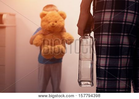 Little scared son covering his face with toy bear from angry drunk mother. Child abuse. Alcoholic addiction. Domestic violence.