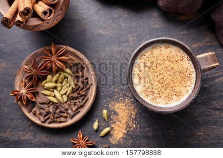 Masala tea chai latte traditional hot Indian sweet milk spiced drink, nutmeg, ginger, cinammon sticks, fresh spices blend, cardamom, anise organic infusion healthy wellness beverage in rustic clay cup