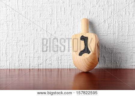 Dreidel for Hanukkah on wooden table against light textured wall