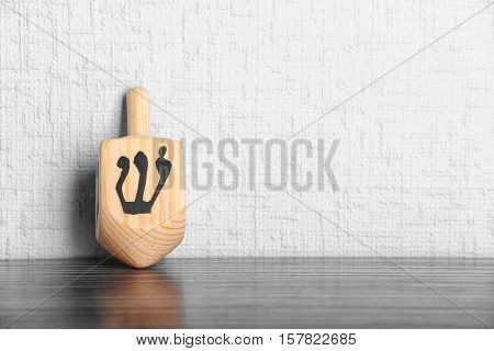 Dreidel for Hanukkah on wooden table against light textured wall