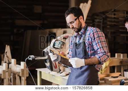 Handsome carpenter in protective glasses standing near his wooden object in the workshop.