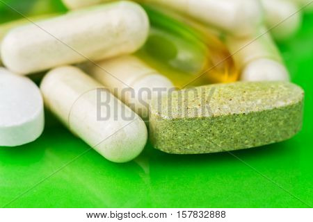 Mixed natural food supplement pills omega 3 calcium multivitamin and glucosamine capsules on green background