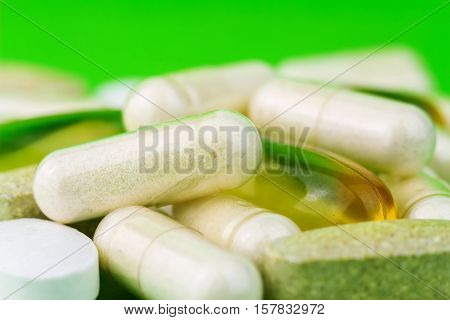 Mixed natural food supplement pills omega 3 calcium multivitamin and glucosamine capsules on green background
