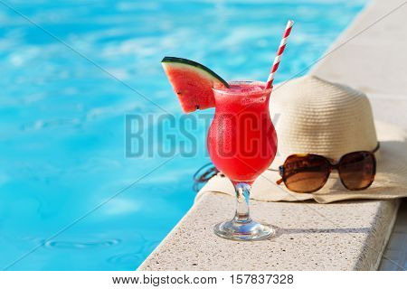 Fresh glass of water-melon smoothie drink with sunglasses, straw hat and slippers on border of a swimming pool - holiday tropical concept