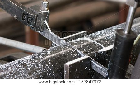 Industrial bandsaw with cooling liquid cutting a steel pipe. Shallow depth of field and motion blur.