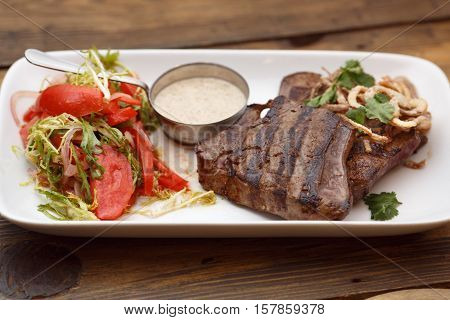 Tasty meat grilled with fresh vegetables with sauce on a plate on a wooden table