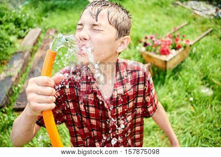 The guy in the wet clothes drinking water from a hose on the farm