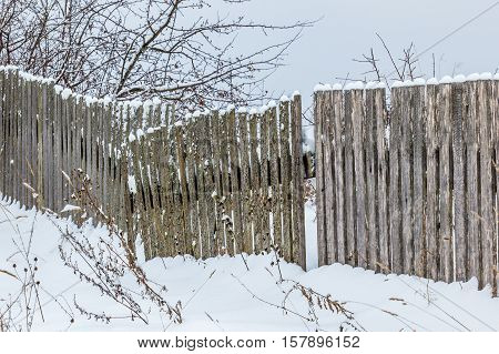 Old wooden fence with snow. Rickety fence after a snowfall.