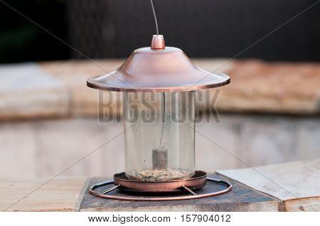 Empty feeder with no seed for bird sitting on a flagstone fire pit.
