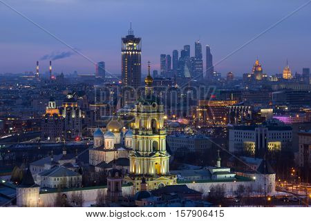 Bell tower of church of St. Sergius of Radonezh of Novospassky Monastery and high buildings in Moscow, Russia at evening