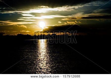 sunset in autumn in November, a bright yellow, brown and black colors, to sit round the sun, clouds heavy different sizes,sun on the horizon,  solar path the pond, very dark background
