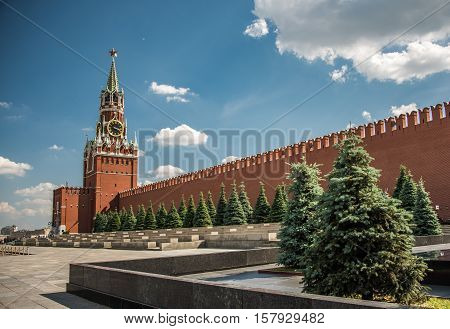 Sunny day at the Red Square with blue sky white clouds green fir-trees the Spasskaya Tower with the Kremlin chimes the main tower with a through-passage on the eastern wall of the Moscow Kremlin