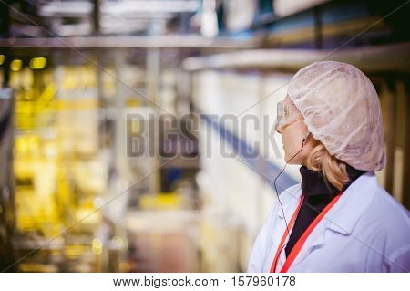 Female Worker On The Production Line Of Beer Factory. Portrait Of A Woman In A White Robe, Standing