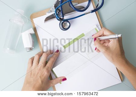 Top view of hands of a female doctor is writing a recipe near a spray inhaler a space chamber and a stethoscope- Medical respiratory disease