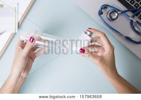 Top view of a close up of the hands of a female doctor is inserting a pressurized cartridge inhaler into an inhalation chamber on a medical demonstration on her desk - Medical respiratory disease