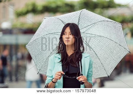 Confident asian girl city portrait. Serious woman outside with umbrella in casual business suite. Beautiful young mixed race Asian Caucasian woman.