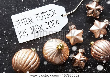Label With German Text Guten Rutsch Ins Jahr 2017 Means Happy New Year 2017. Bronze Christmas Tree Balls On Black Paper Background With Snowflakes. Christmas Decoration Or Texture. Flat Lay View
