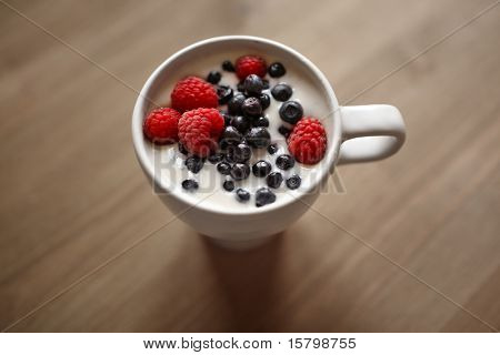 Tasse Joghurt mit frischen Bio Himbeeren und Heidelbeeren auf Whooden Tisch. Nahaufnahme, flachen Dof.