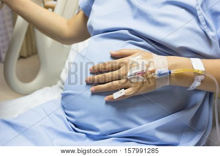 Asian Pregnant Woman patient is on drip receiving a saline solution on bed VIP room at hospital selective focus.