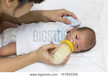 Asian cute new born baby eatting mlik mother in bottle mum feeding on white towel background.