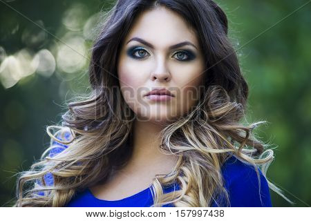 Young beautiful plus size model in blue dress outdoors confident woman on nature professional makeup and hairstyle close-up portrait sunbeams background
